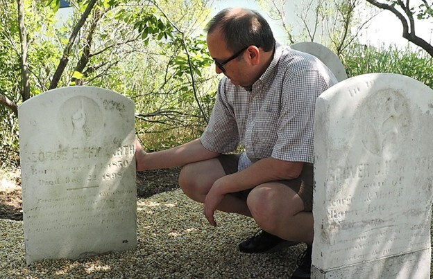 Lee Howeth kneels beside family gravestone