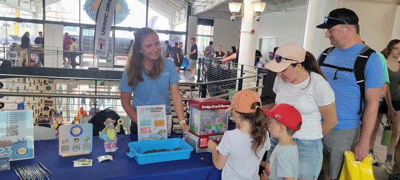Image of MPA representative behind a table, with a small claw machine game being played by two young children and two adults. 