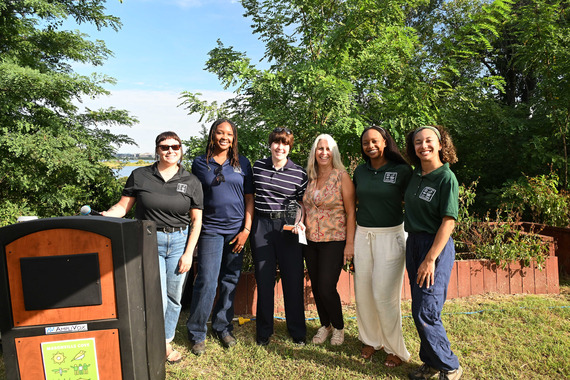 Group of people wearing shirts that say "Friends of Masonville Cove" standing outside in a garden with the Baltimore Harbor visible in the back. 