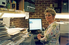 ann baker, standing at her desk, looking over her shoulder at the camera