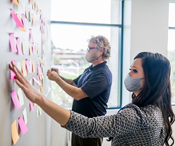 two educators placing post-it  notes on a wall