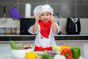 Cute Asian girl wear chef uniform with a lot of vegetables on the table in the kitchen room
