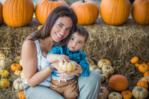 Fotografía de un padre sosteniendo a su hijo y sonriendo en un huerto de calabazas.