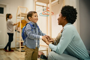 Photo of child smiling and holding hands with his mother at school or child care.