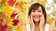 Photo of woman smiling and touching faces near autumn leaves.