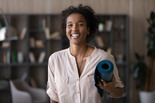 Photo of smiling woman holding rolled-up yoga mat.