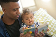 Foto de un padre leyendo un libro a un bebé en su regazo en casa.