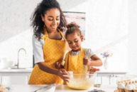 Fotografía de un padre cocinando y revolviendo con una niña pequeña en la cocina de casa.