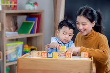 Child and parent smiling playing with toy blocks at home.