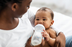 Photo of parent smiling and feeding a baby a bottle.