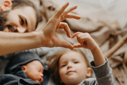 Photo of parent making heart shape hand gesture with child while playing.