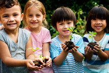 Photo of young children smiling and holding soil and plants.