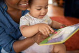 Photo of parent holding baby in lap and reading picture book.
