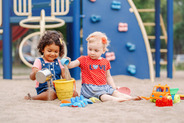 Photo of two babies playing together in playground sand outside.