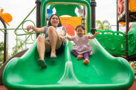 Foto de un padre y un hijo sonriendo y bajando por un tobogán en un parque infantil.