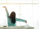 Person waking up in bed and stretching, looking outside at sunny morning.