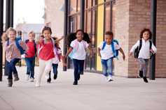 Niños corriendo con mochilas fuera de la escuela primaria.
