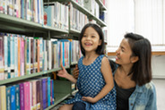 Madre e hija sonriendo frente a una estantería de la biblioteca.