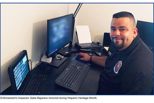 Enforcement’s Inspector Gabe Bejarano honored during Hispanic Heritage Month, sitting at desk with computer and electronics.