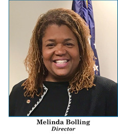 DPIE Director Melinda Bolling, wearing black suit with white trim, US flag in background