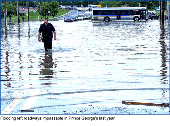 Flooding left roadways impassable in Prince George’s last year, picture of police officer wading through 2 feet of water across intersection
