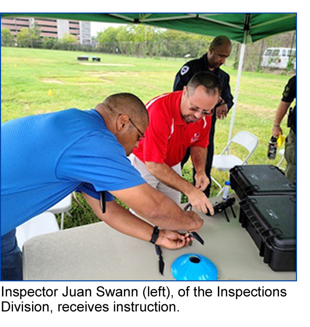 Inspector Juan Swann (left), of the Inspections Division, receives instruction on preparing a drone flight