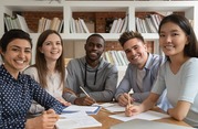 diverse group of smiling interns seated around a table with pens and paper