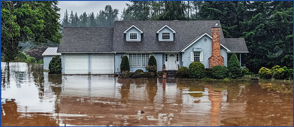 Blue country manor style house in a flood with water levels up to the garage and house doors