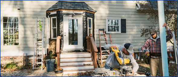 Workers fixing front doorway with windows and framework on a house
