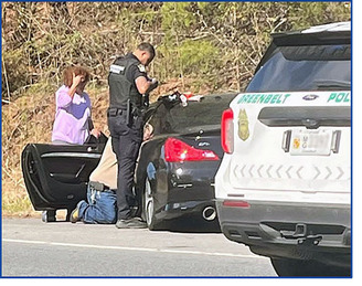 Charles Graham kneeling at car door to assist driver suffering a medical emergency with bystander and police officer writing report
