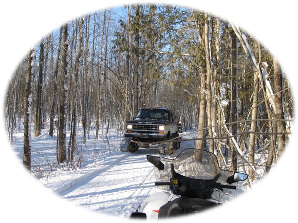 Snowmobile and trail groomer passing each other on trail from riders perspective.