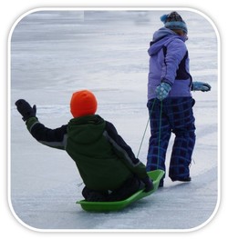 Sled with child in being pulled across ice by another.