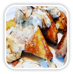 French toast golden browned with drizzled with whipped cream and maple syrup and topped with sliced almonds.