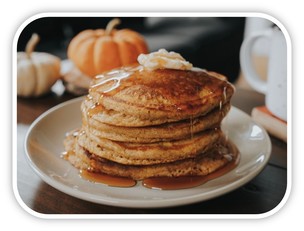 Pumpkin pancake stacked on plate with syrup and butter.