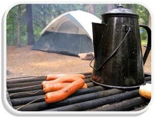 Campsite photo showing grill with franks and coffee pot with dome tent in background.