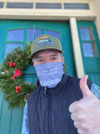 Andy Cutko in front of a green door with holiday wreath and wearing an ATV COVID mask and a Maine State parks cap.