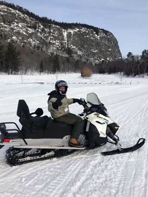 Andy Cutko, BPL Director, on snowmobile  with Mt. Kineo in background.