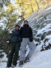 Andy and Haven on hike at Little Concord Pond, Maine. Rock ledge with an ice sheet and  lots of icicles in the background.