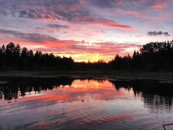 Sunrise reflection on lake of orange-reds and golds with a light purple sky. 