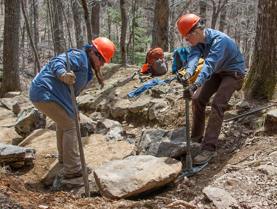 Trail work showing two MCC trail crew moving a boulder.