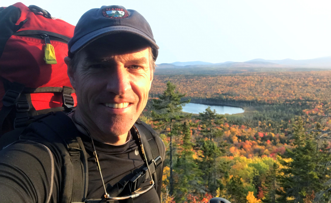 Andy Cutko on Great Circle Trail of Nahmakanta Public Land showing Third Musquash Pond and autumn foliage of forest in background.
