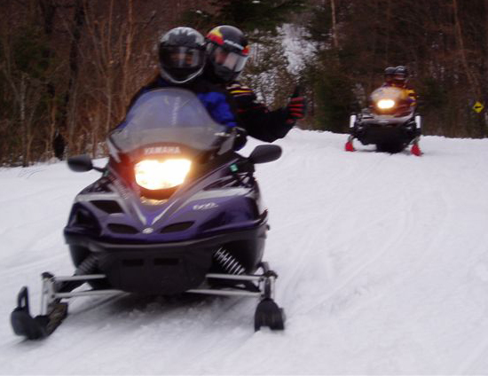 Snowmobiles on a groomed forest trail.