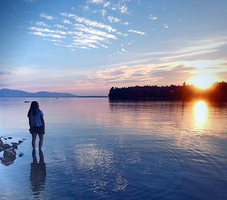 A girl watching the sunset over the water at Lily Bay State Park, Maine.