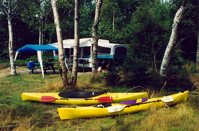 Campsite set up with a pop-up camper and two kayaks on the foreground.
