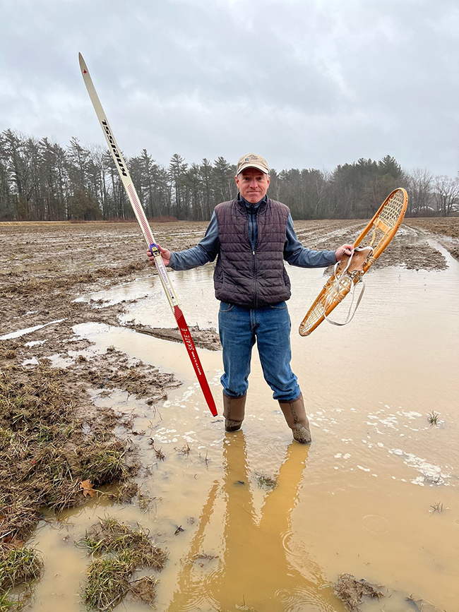 Waiting for Winter - Andy Cutko in muddy field during mid-January with xc-ski in one hand and snowshoe in the other.