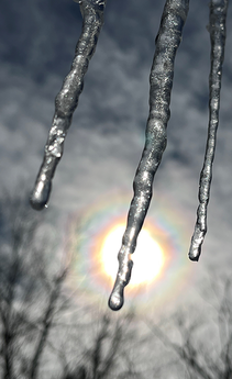 Three icicles with partly cloudy sky and the sun in the background.