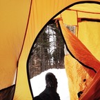 Winter camping image taken from inside a yellow dome tent looking out the tent door at the snow and woods.