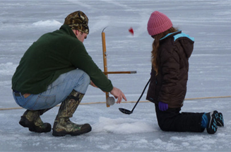 Man and young girl setting and ice fishing trap.