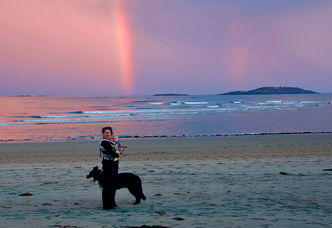 Woman, child, and dog at Popham Beach with ocean and rainbow in background. Photo by Sean Vaillancourt.