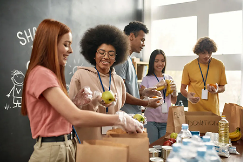 Happy young volunteers in gloves collecting, sorting food for needy people, courtesy of Adobe Stock.